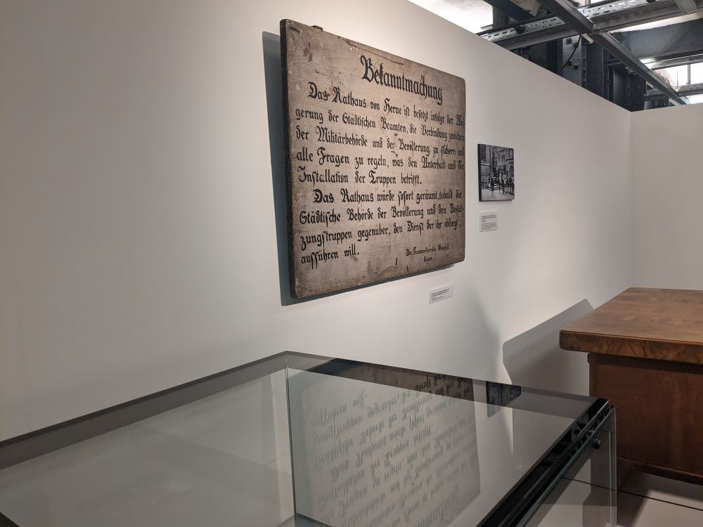 Schild an der Wand mit einer Bekanntmachung über die Besetzung des Rathauses in Herne durch Besatzungssoldaten.